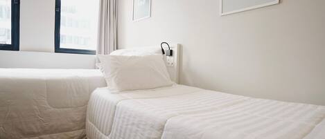 Una habitación de hotel con dos camas individuales, una ventana con cortinas, un enchufe en la pared y una cita enmarcadas en la pared.