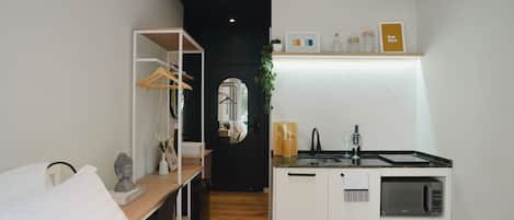 Habitación de hotel pequeña con cama, kitchenette, espejo y repisa con adornos.