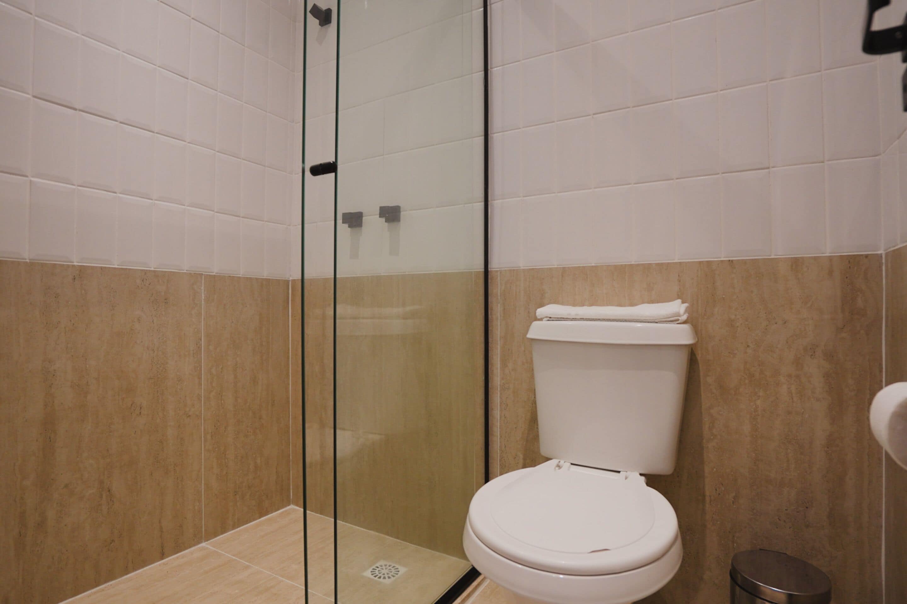 A modern bathroom with a glass shower enclosure, a white toilet, and beige tiled walls.