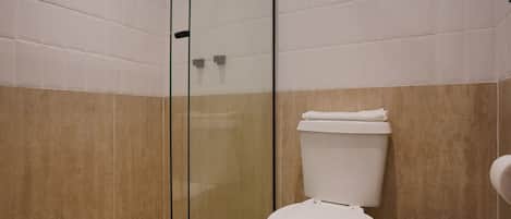A modern bathroom with a glass shower enclosure, a white toilet, and beige tiled walls.