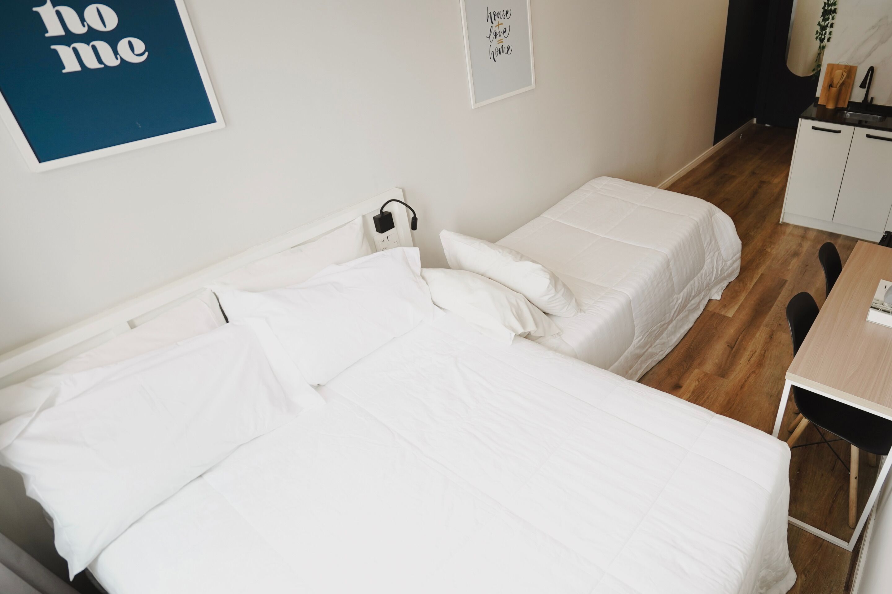 A bedroom with two single beds, a desk, and a small kitchenette.