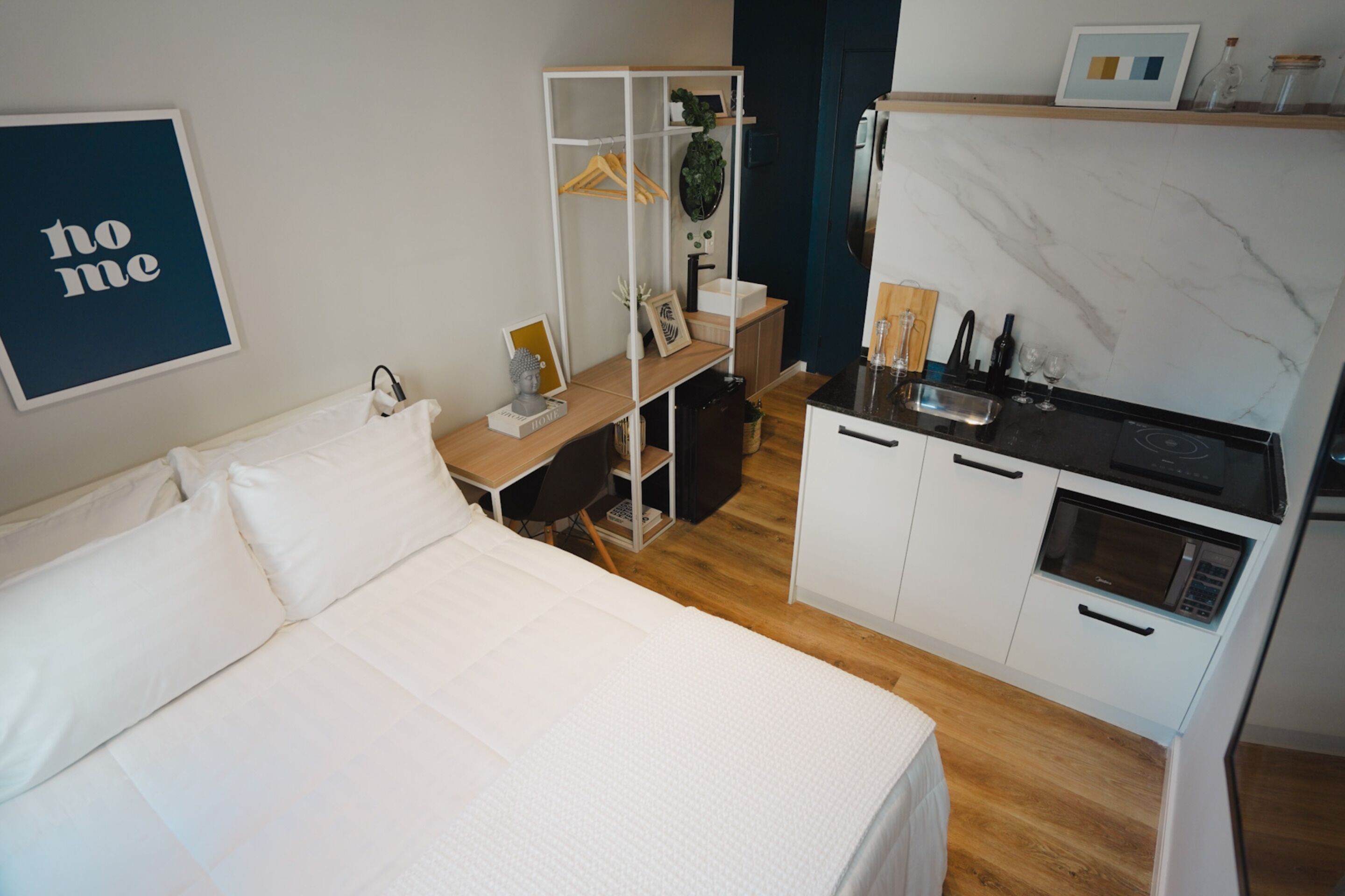 A compact room with a bed, a kitchenette, and a small desk.