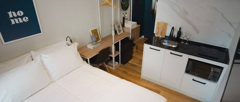 Quarto compacto com cama, cozinha compacta e pequena escrivaninha.