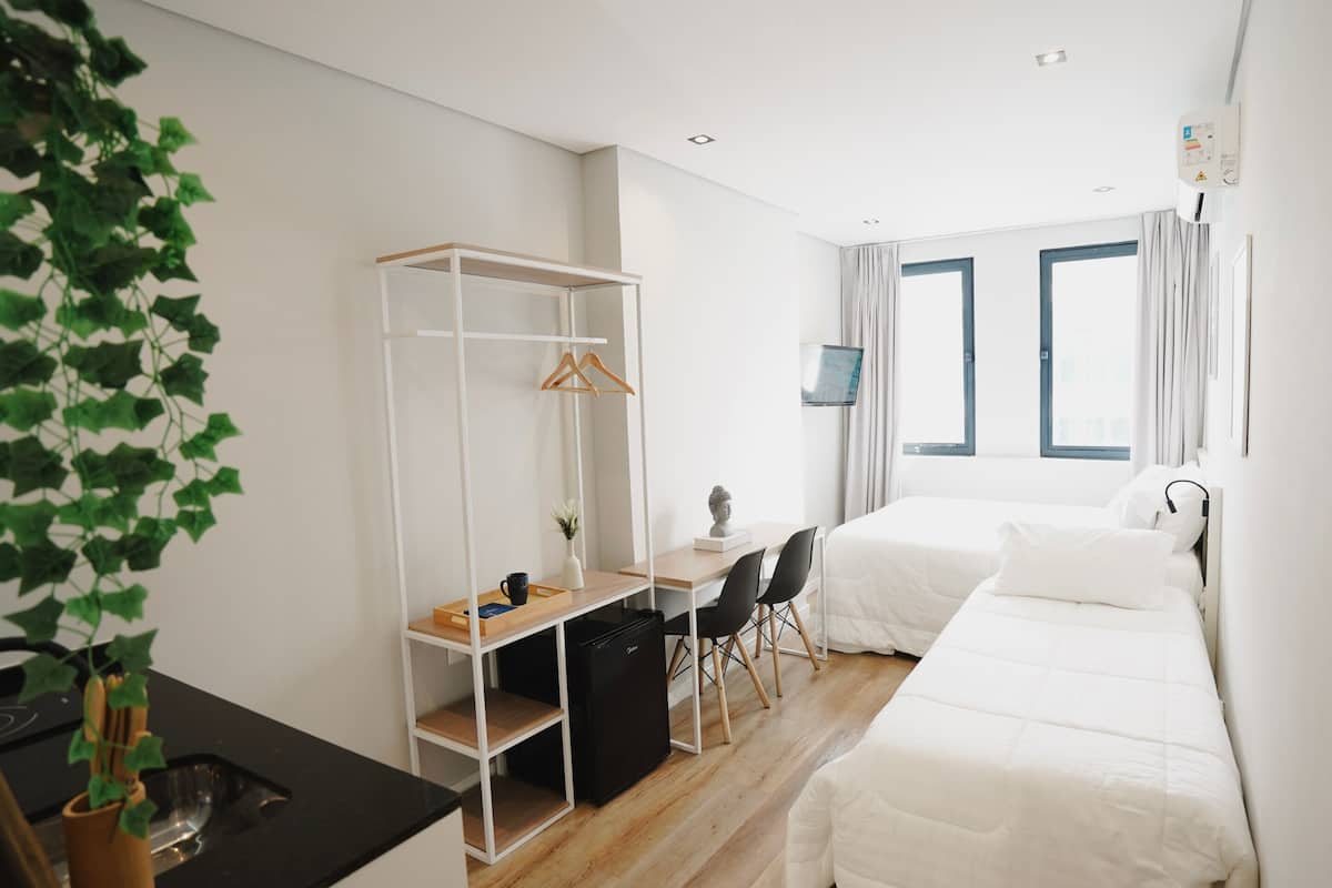 Ein Hotelzimmer mit einem Bett, einem Schreibtisch mit Stuhl, einem Kleiderschrank, einer kleinen Kühlschrank und einer Pflanze.