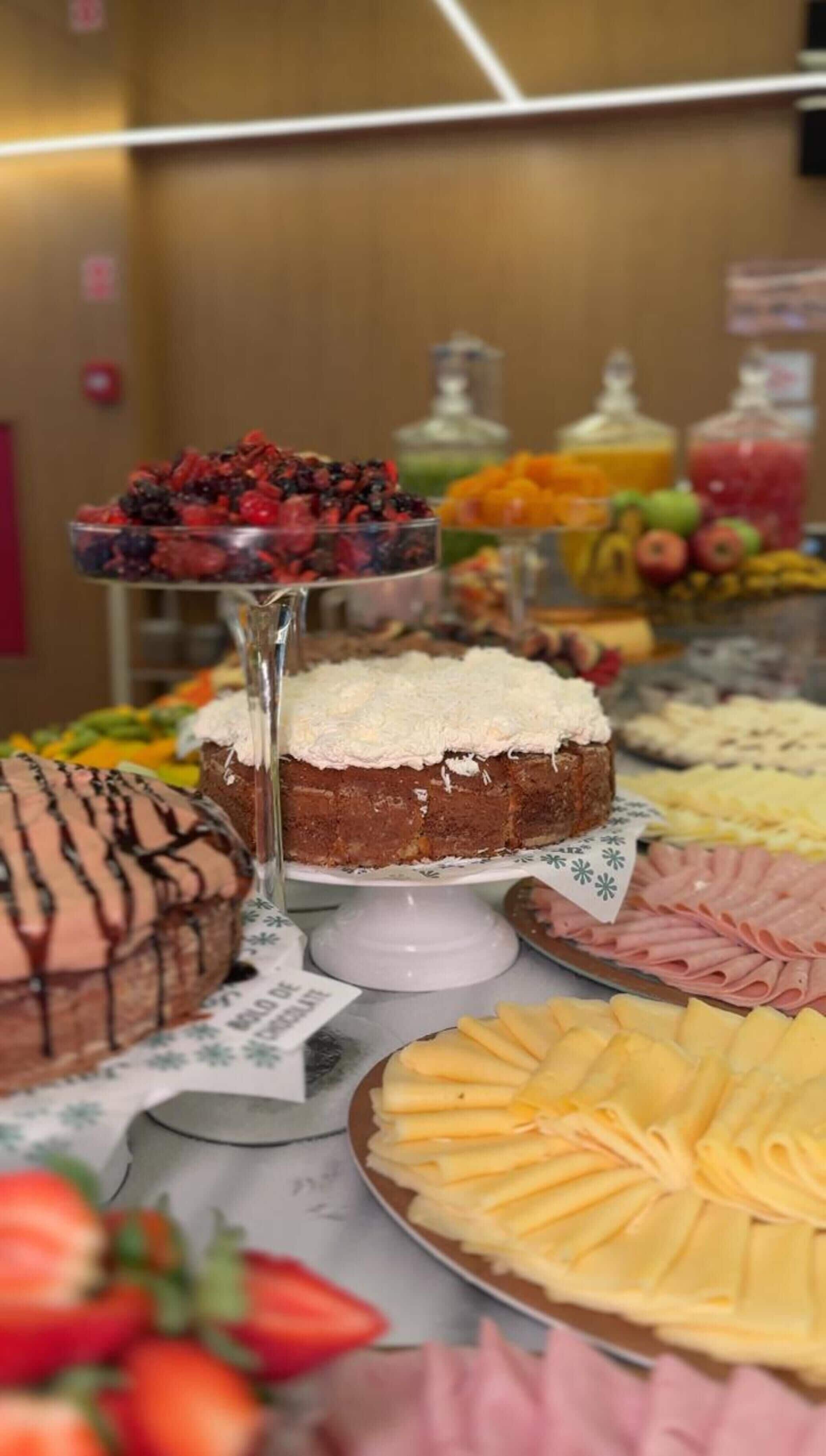 A buffet with various food items including a cake with white frosting, a chocolate cake with chocolate drizzle, and a variety of fruits and cheeses.