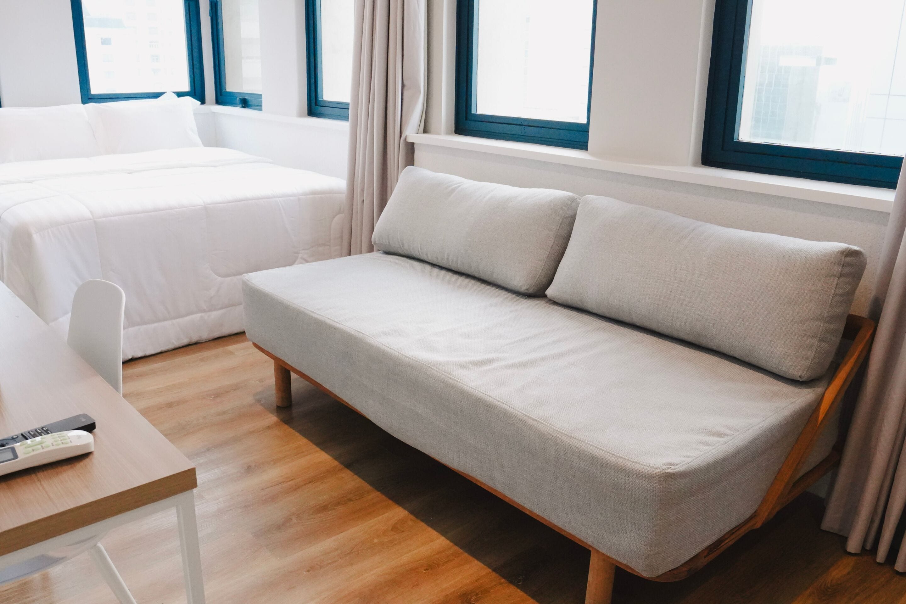 A modern hotel room with a sofa, a bed, a desk, and a window with curtains.