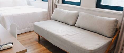A modern hotel room with a sofa, a bed, a desk, and a window with curtains.