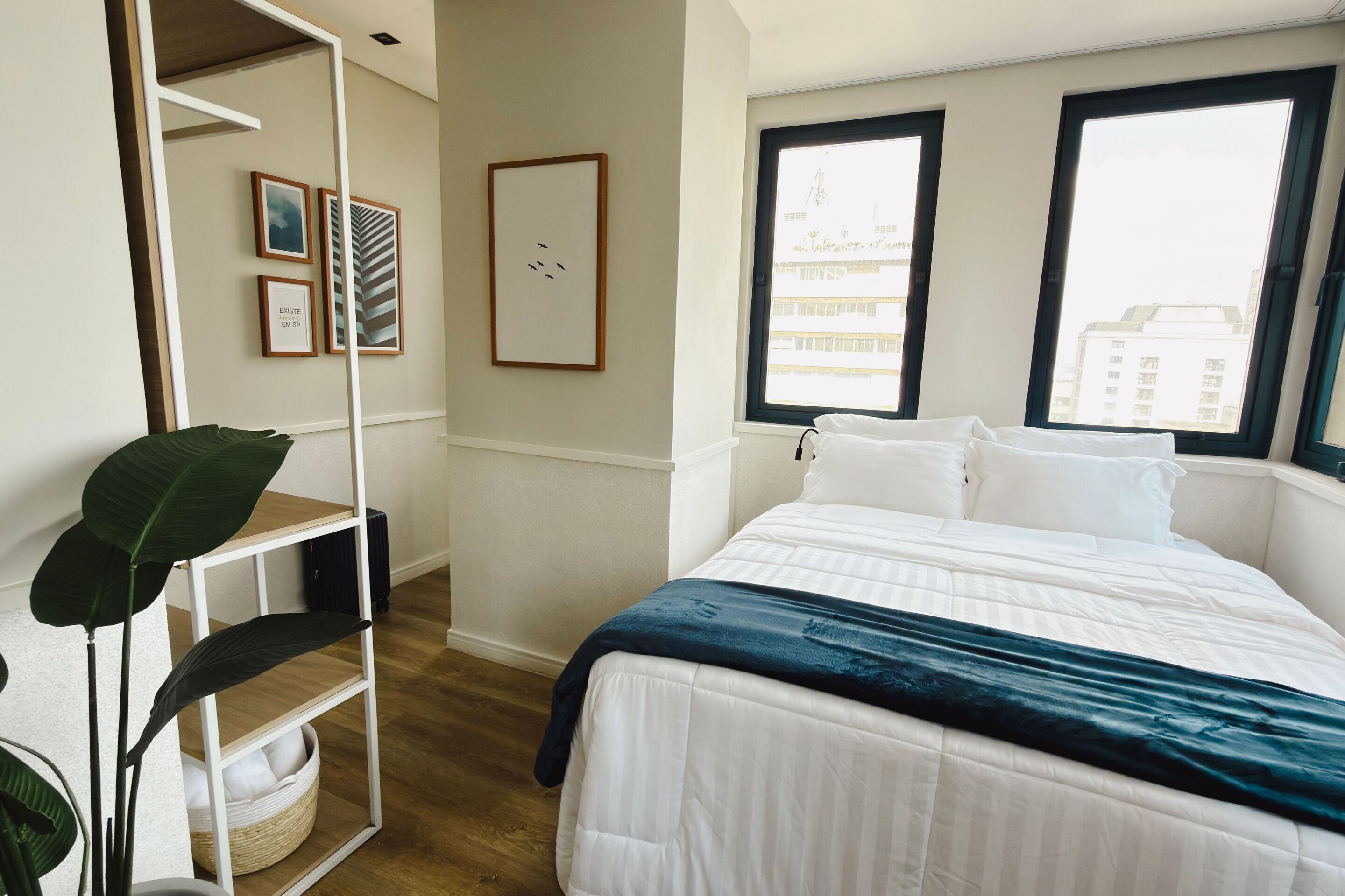 Une chambre à coucher avec un lit, une fenêtre, une plante et une étagère fixée au mur.