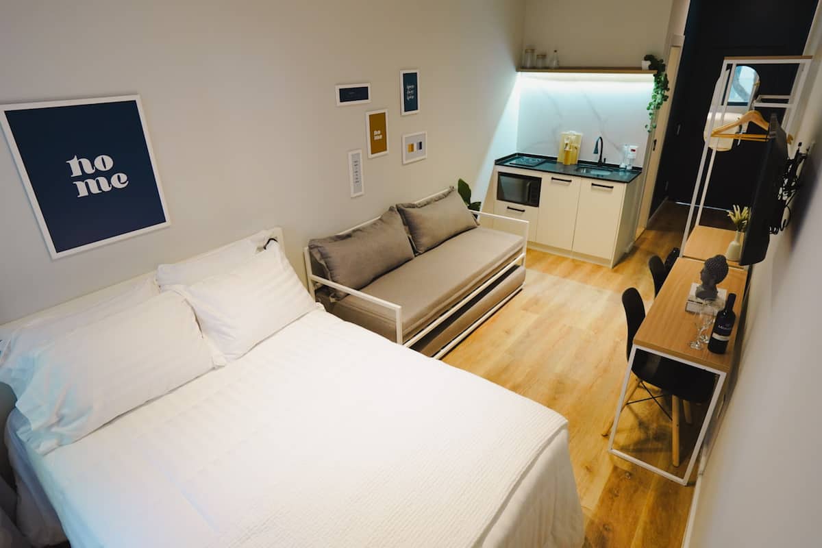 Ein gemütliches Schlafzimmer mit Bett, Schlafsofa, einer kleinen Küchenzeile und einem Schreibtisch mit Stuhl.