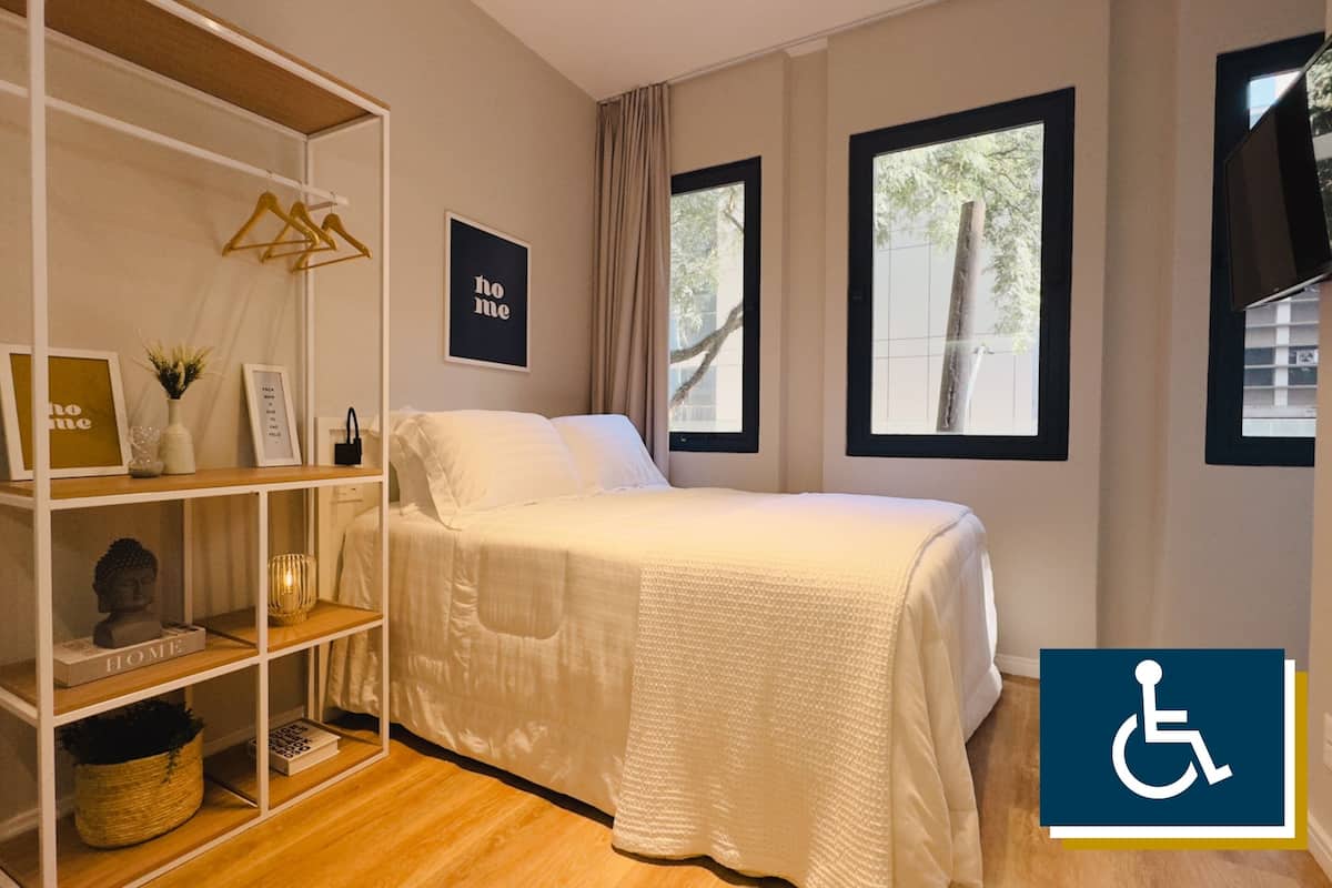 Ein Schlafzimmer mit einem Bett, einem weißen Regal mit Dekoration und zwei mit Vorhängen versehenen Fenstern.