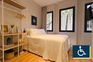 A bedroom with a bed, a white shelf with decorative items, and two windows with curtains.