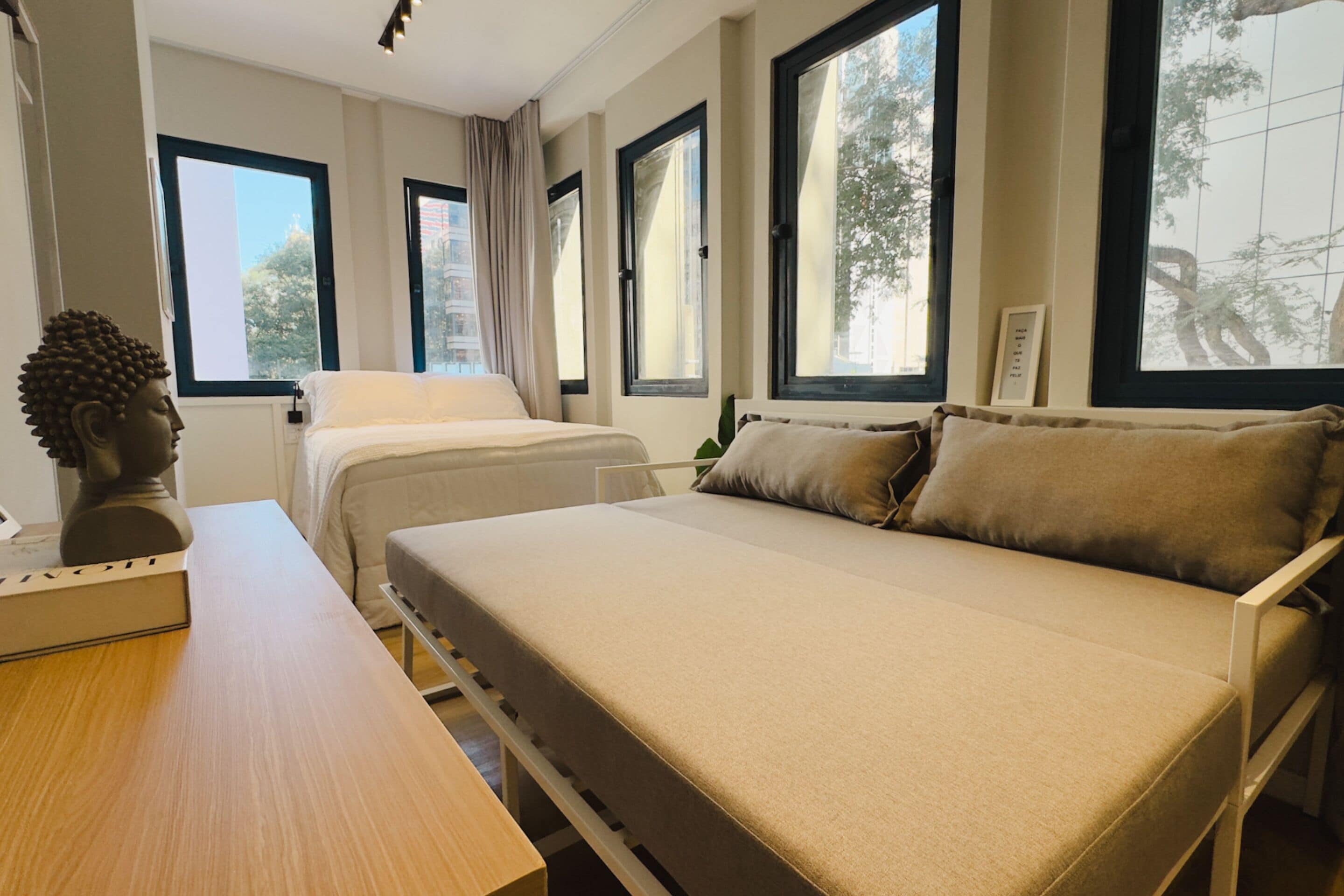 Ein Zimmer mit zwei Betten, einem Holztisch und großen Fenstern mit Vorhängen.