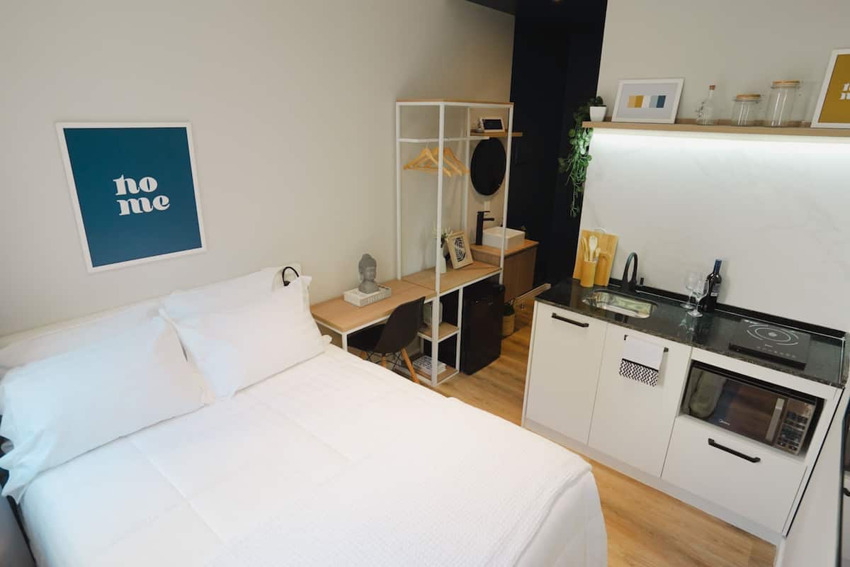 Ein kleines Hotelzimmer mit Bett, Schreibtisch, Spiegel, einer kleinen Küchenzeile und einem Schild mit der Aufschrift 'bitte nicht stören'.