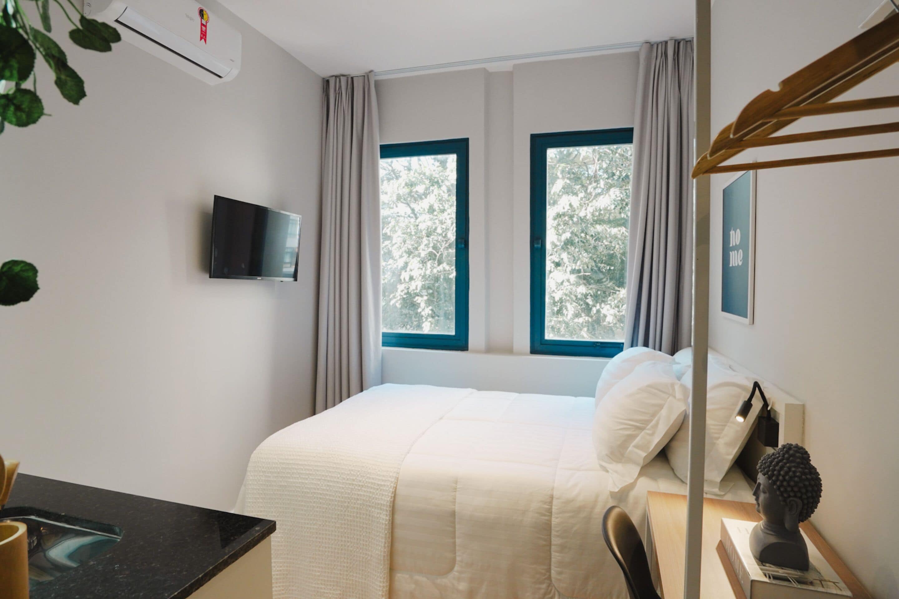 A hotel room with a bed, a desk, a TV, and a window with curtains.