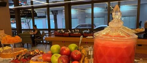 Una mesa de buffet con diversas frutas, postres y un gran bol de ponche de vidrio.