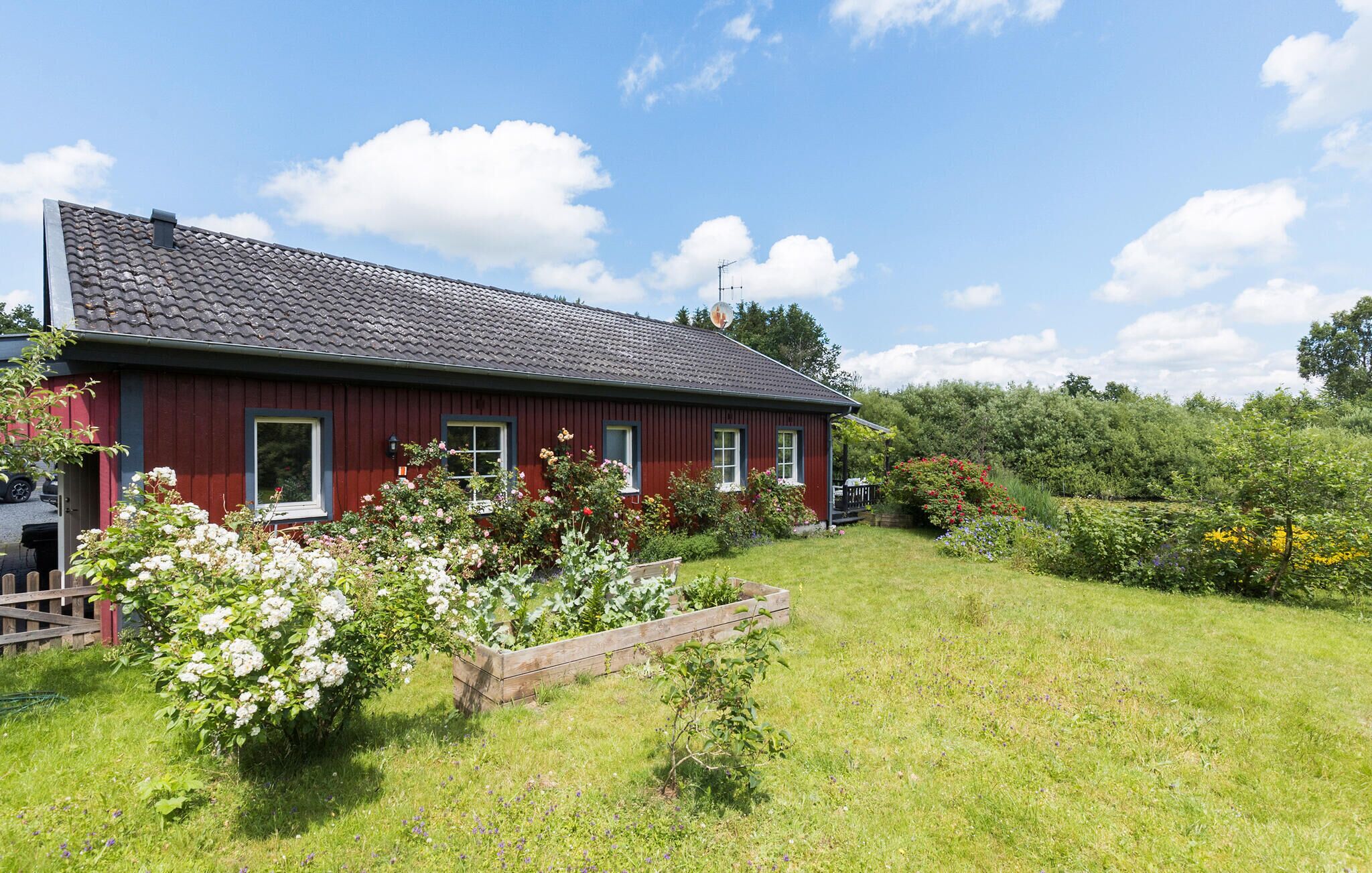 Ett rött trähus med ett tak täckt av tegelpannor, omgivet av en välskött trädgård med olika växter och blommor.