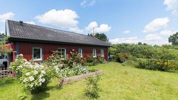 Ett rött trähus med ett tak täckt av tegelpannor, omgivet av en välskött trädgård med olika växter och blommor.
