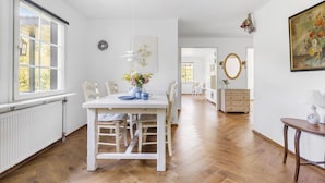 A spacious room with a wooden floor, a white dining table with chairs, a dresser, and a mirror.