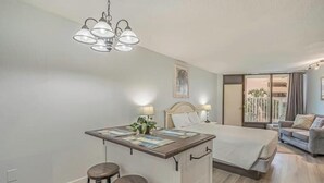 Et hotelværelse med seng, en lille bar med barstole, en loftlampe og udsigt til balkonen.