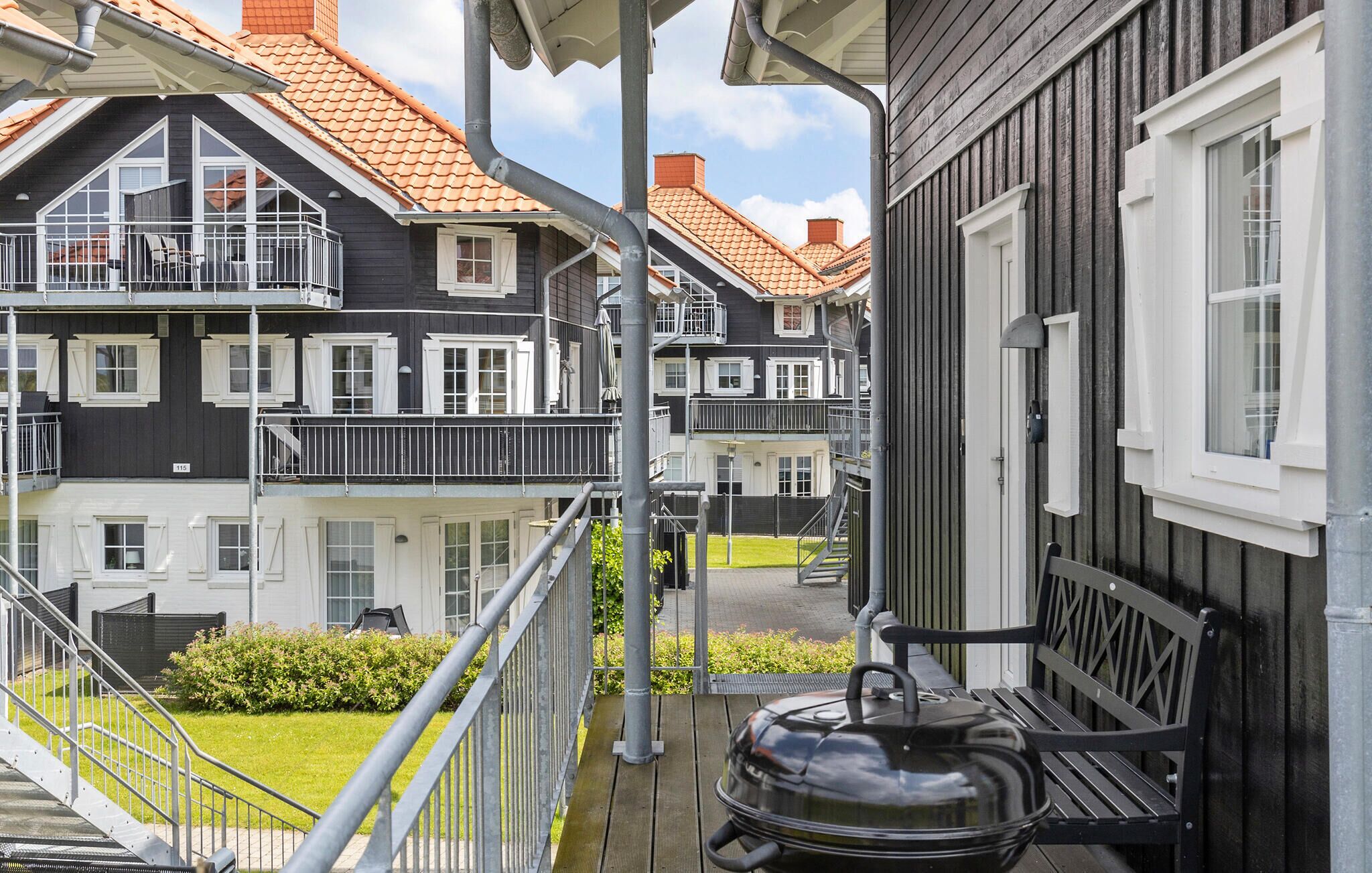 En bostadsbyggnad med balkong, grill och en välskött trädgård.