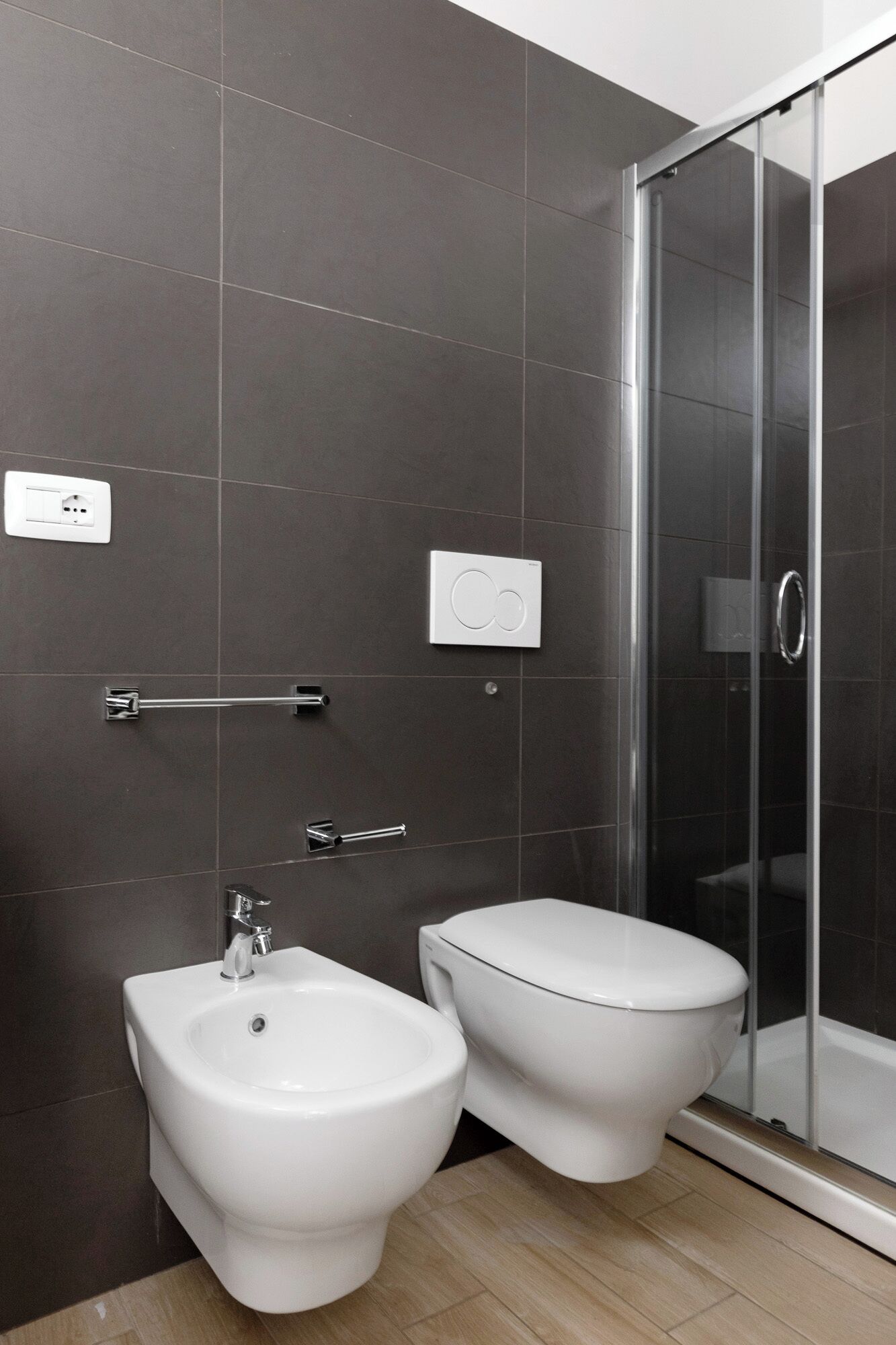 Ein modernes Badezimmer mit dunklen Fliesen, einer Duschkabine aus Glas, einem Bidet und einer Toilette.