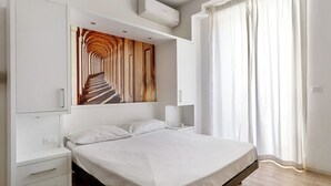 Ein modernes Schlafzimmer mit einem großen Bett, einem Kleiderschrank, einem Nachttisch, einer Wand-Klimaanlage und einem Fenster mit Vorhängen.