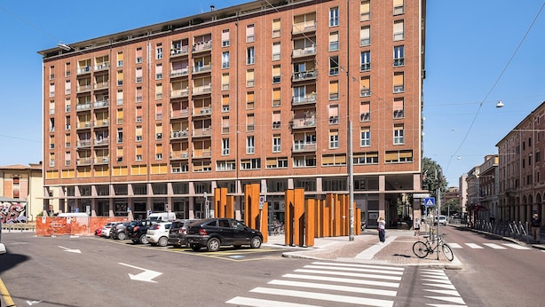 Ein mehrgeschossiges Wohnhaus mit Balkonen, einer Fußgängerzone und parkenden Autos.