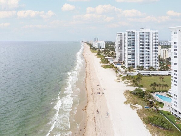 A beachfront hotel with multiple high-rise buildings, a sandy beach, and a pool area.
