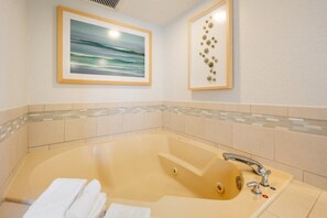 A bathroom with a large bathtub, a sink with a modern faucet, and a framed painting of a seascape. - Pompano Beach | Couples Ocean Weekend | Pool + Beach (Pompano)
