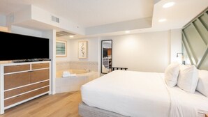 Une chambre d’hôtel moderne dotée d’un grand lit, d’une télévision à écran plat, d’une baignoire intégrée et d’un design minimaliste.