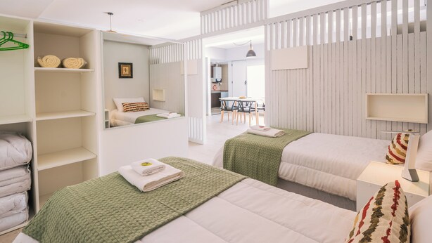 Habitación de hotel con dos camas, zona de comedor y baño visible a través de una puerta abierta.