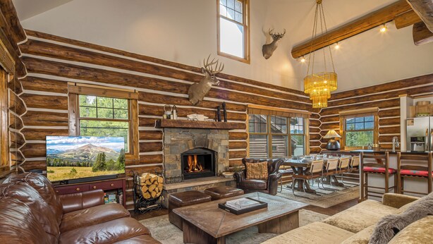 A log cabin interior with a stone fireplace, leather furniture, and mounted deer heads.