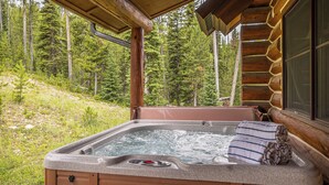 A hot tub with a control panel, surrounded by a wooden cabin structure, set against a forest backdrop.