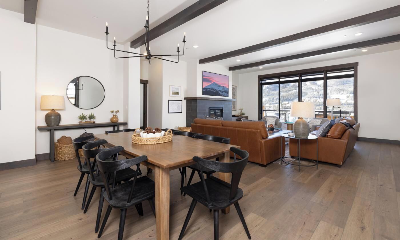 Un salon moderne avec une table à manger en bois, des chaises noires, une cheminée et une grande fenêtre donnant sur un beau paysage.