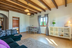 A living room with a sofa, a dining table with chairs, a white cabinet, and a window with curtains. - Finca Can Grau (Sencelles)