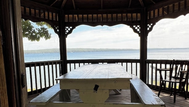 Un pabellón de madera con mesa de picnic, con vista a un cuerpo de agua.