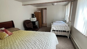 Una habitación de hotel con una cama grande, una cama más pequeña, un escritorio con una silla y un armario.