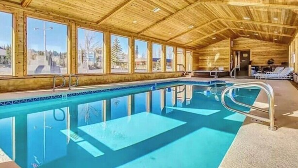 Una piscina interior de madera con ventanas transparentes, sillones de descanso y suelo de baldosas.