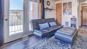 Una sala de estar moderna con un sofá de cuero, un reposapiés a juego y un amplio ventanal con vistas a un paisaje nevado.