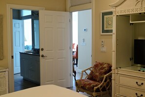Une chambre à coucher comprenant un lit, une chaise, une commode et une porte donnant sur une autre pièce.