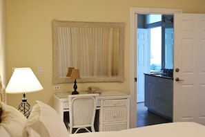 Ein Hotelzimmer mit einem Bett, einem Schreibtisch mit Lampe, einem Telefon, einem Korbstuhl, einem Spiegel und einer Tür zu einem Badezimmer.