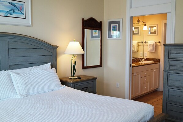 A hotel room with a bed, bedside lamp, mirror, and a bathroom with a sink and cabinets.