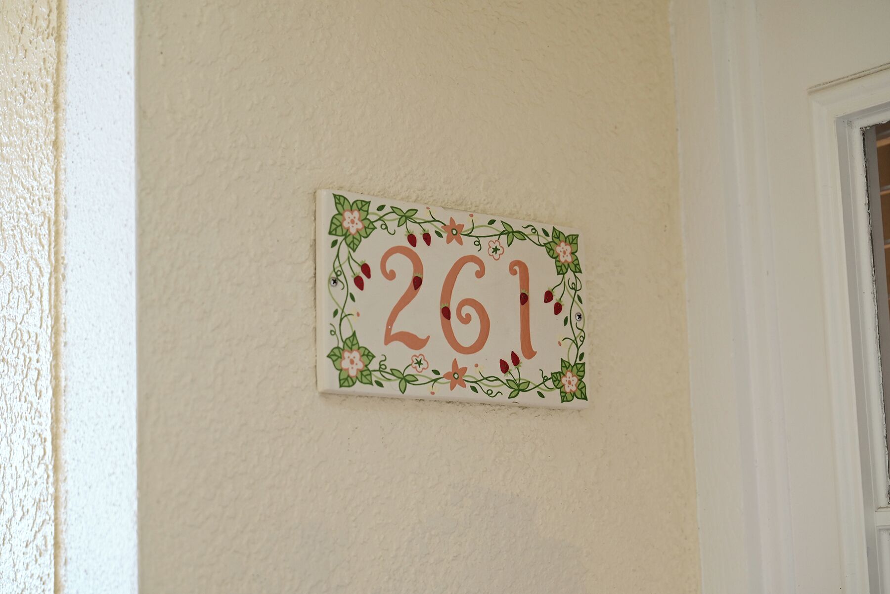 A wall-mounted sign with the number '261' surrounded by floral and berry designs.