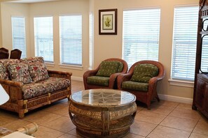 A living room with a patterned sofa, two armchairs, a glass coffee table, and a framed picture on the wall. - Spacious One-Bedroom Condo with Island Comforts (Bradenton Beach)