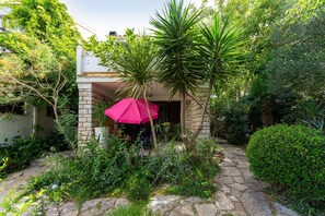 A stone pathway leading to a building with a pink umbrella, surrounded by lush greenery and various plants. - Fantastic Garden Zoey 4 (Novalja)