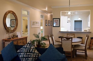 A dining area with a round table, chairs, a mirror, and framed artwork on the walls. - Spacious One-Bedroom Condo with Island Comforts (Bradenton Beach)