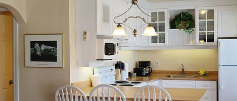 A kitchen with white cabinetry, a hanging light fixture, a framed picture on the wall, and a wooden island with chairs.