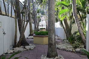 Un chemin bordé d’arbres et d’une clôture blanche, qui mène à un bâtiment à la façade blanche et doté d’un balcon.