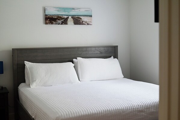 A bed with a wooden headboard, white bedding, and a painting of a beach scene on the wall.