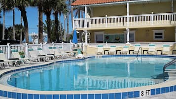 A swimming pool with a 3 ft 6 in depth and 8 ft width, surrounded by lounge chairs and a building with a red-tiled roof.